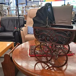 Antieke kinderwagen met houten decoratief frame en rode wielen, op een houten tafel in de winkel