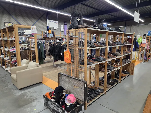 Winkelvloer met houten stellingen vol tweedehandsartikelen, kleding aan rekken en zitbank in de kringloopwinkel