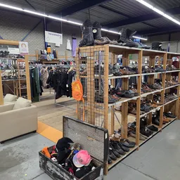 Winkelvloer met houten stellingen vol tweedehandsartikelen, kleding aan rekken en zitbank in de kringloopwinkel