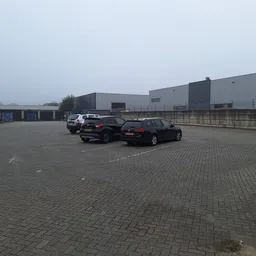 Parkeerterrein met enkele auto's en industriële gebouwen op de achtergrond