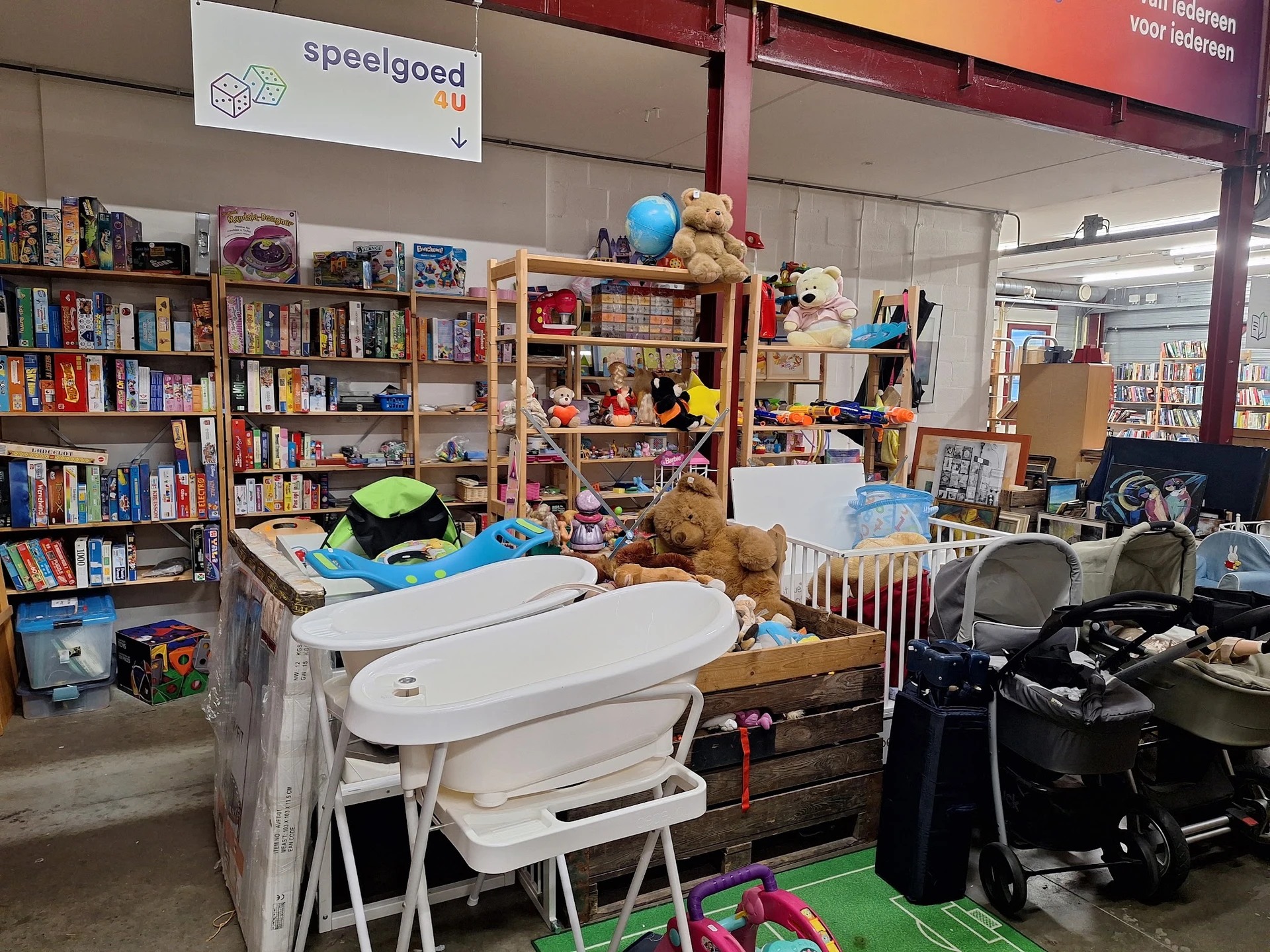 Winkelvloer met stellingen vol boeken, speelgoed, kindermeubels en huishoudartikelen in een kringloopwinkel