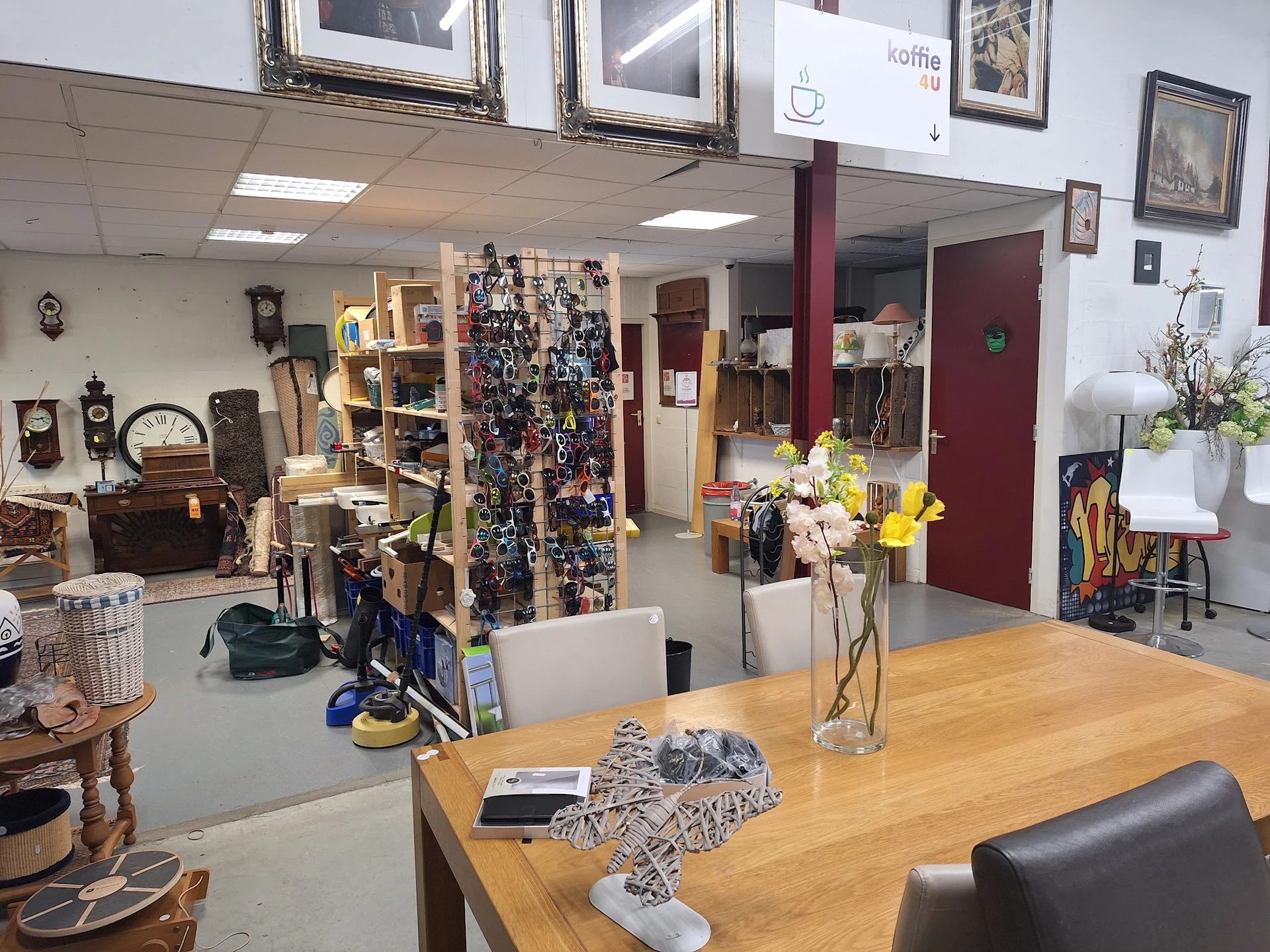 Overzicht van de winkelvloer met houten tafel, diverse artikelen, stellingen met spullen, bloemen in vazen en verschillende i