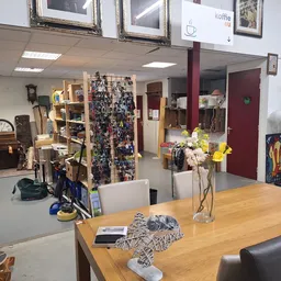 Overzicht van de winkelvloer met houten tafel, diverse artikelen, stellingen met spullen, bloemen in vazen en verschillende i