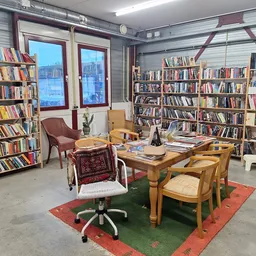 Leesruimte in kringloopwinkel met boekenkasten, houten tafel, stoelen en uitzicht op ramen
