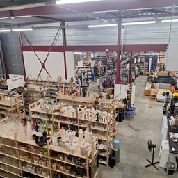 Overzicht van de kringloopwinkel met houten stellingen vol spullen, klanten kijken rond en verschillende afdelingen in de rui