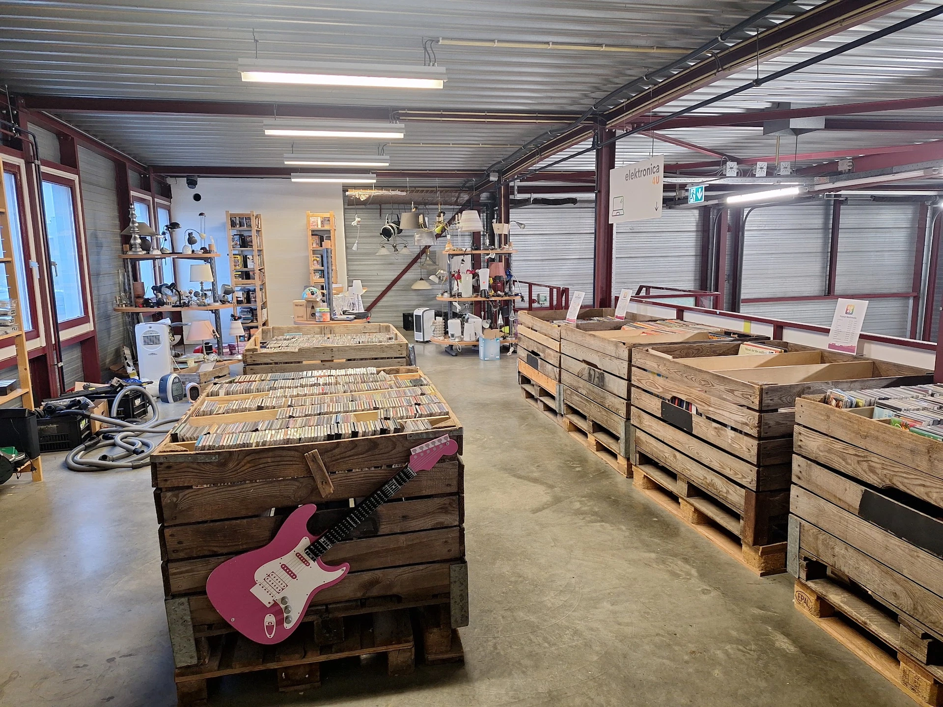 Ruim magazijn met houten pallets en een roze elektrische gitaar op werkbank, werkplaats van kringloopwinkel