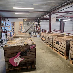 Ruim magazijn met houten pallets en een roze elektrische gitaar op werkbank, werkplaats van kringloopwinkel