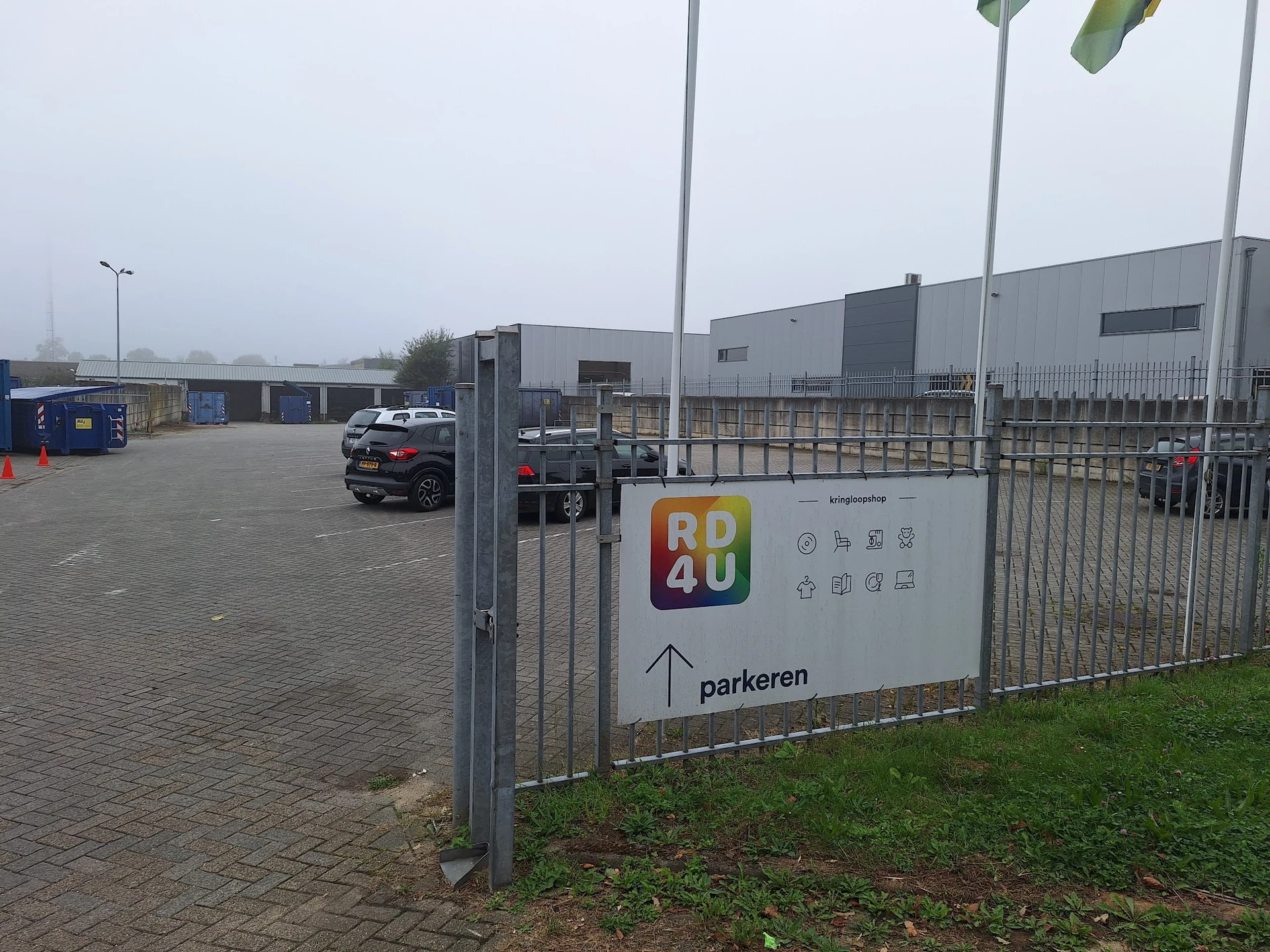 Parkeerterrein met informatiezuil van RD4U kringloopshop en grijs bedrijfsgebouw op achtergrond