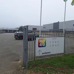 Parkeerterrein met informatiezuil van RD4U kringloopshop en grijs bedrijfsgebouw op achtergrond