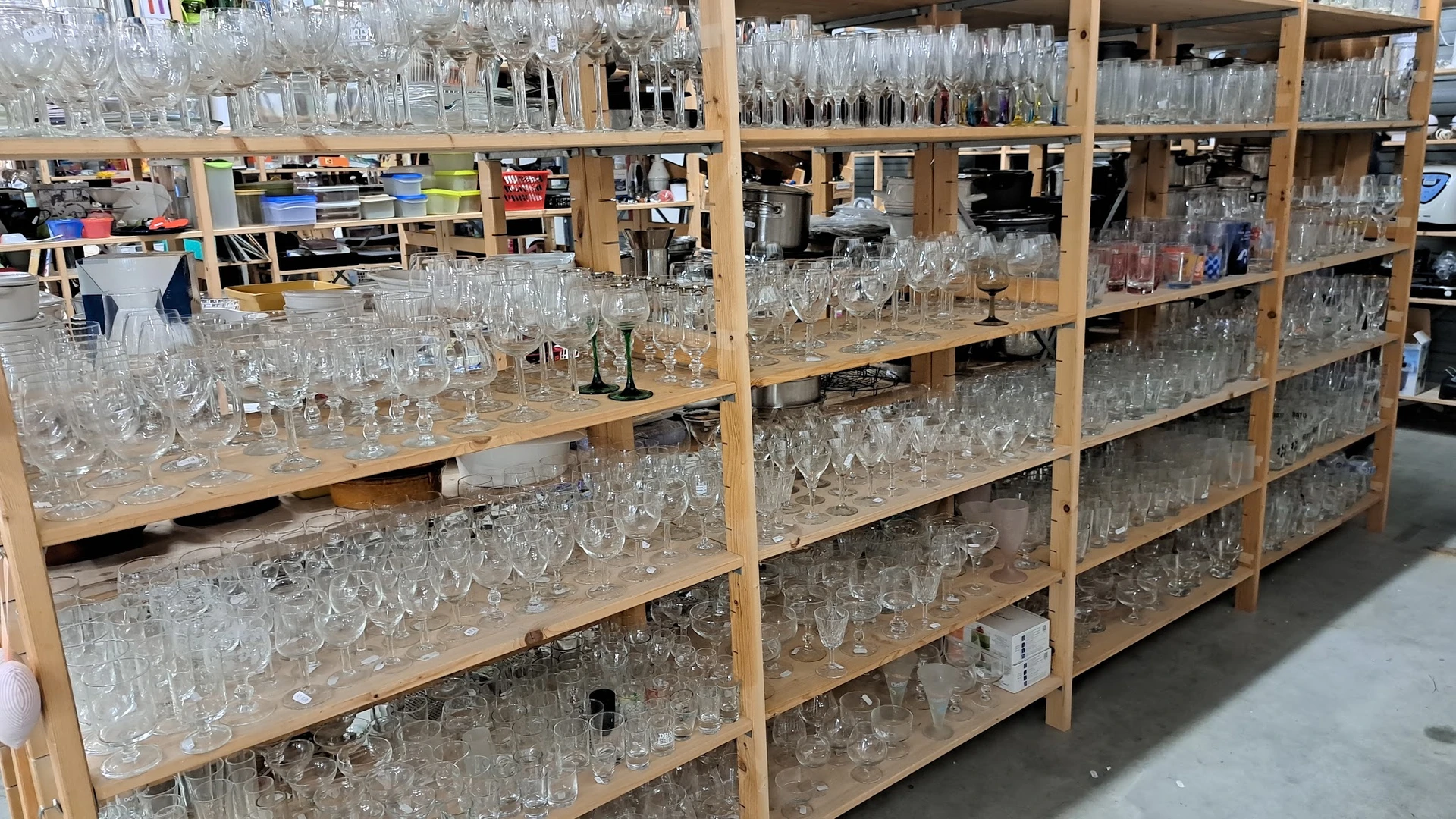 Houten stellingen vol glazen drinkglazen en serviezen in verschillende soorten en maten
