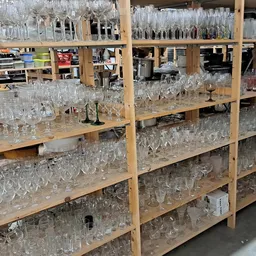 Houten stellingen vol glazen drinkglazen en serviezen in verschillende soorten en maten