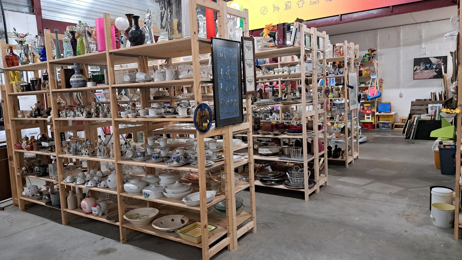 Houten stellingen met huishoudelijke artikelen, servies en decoratiespullen in de kringloopwinkel