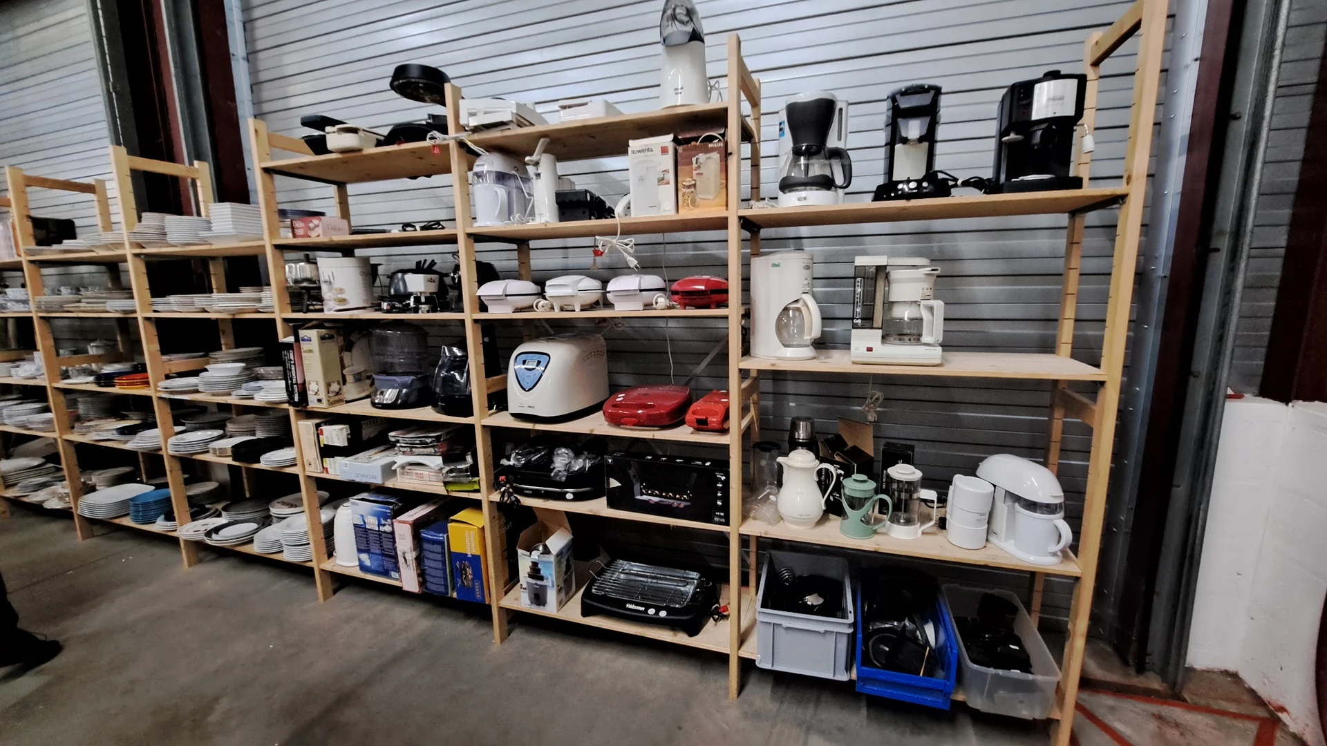 Houten stellingen vol met huishoudelijke apparaten, keukenspullen en elektronica in de kringloopwinkel