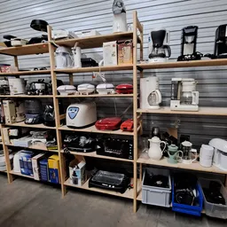 Houten stellingen vol met huishoudelijke apparaten, keukenspullen en elektronica in de kringloopwinkel