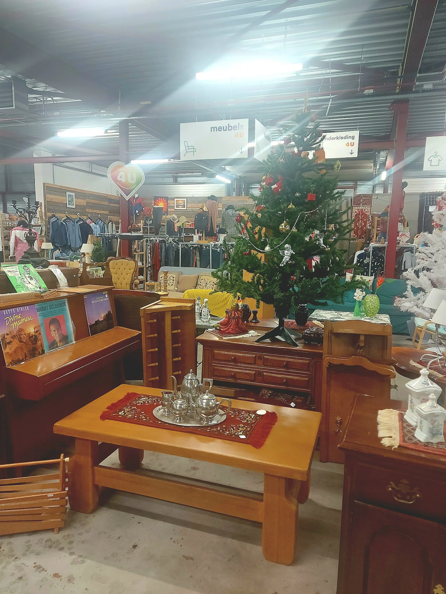Winkelvloer met houten meubels, kerstboom, kledingrekken en diverse spullen in kringloopwinkel