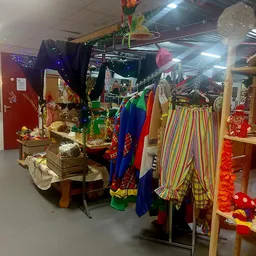 Rekken met kleurrijke carnavalskostuums en -attributen, waaronder clownspakken en regenbooggestreepte broeken in de kringloop