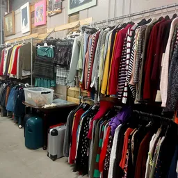 Rekken met tweedehands kleding, jassen en truien in verschillende kleuren georganiseerd in de winkel
