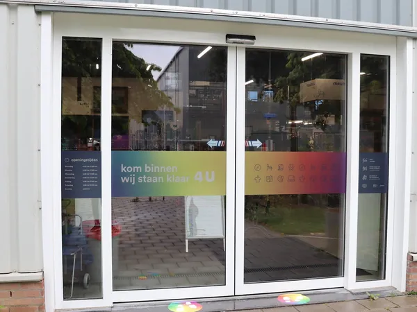 Witte aluminium glazen voorgevel van een kringloopwinkel met gekleurde raamstickers en binnenzicht
