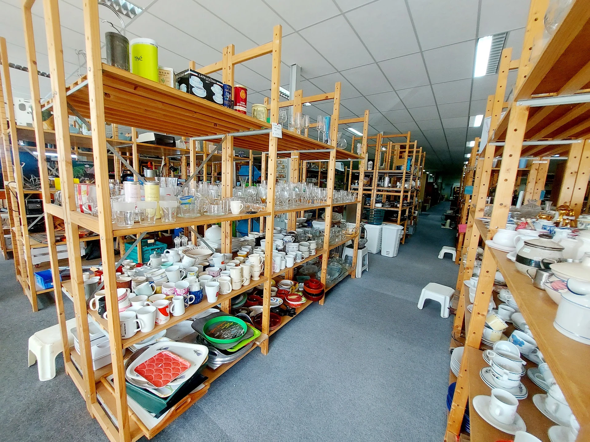 Houten stellingen met wit servies, glazen en huishoudartikelen in de kringloopwinkel