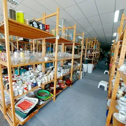 Houten stellingen met wit servies, glazen en huishoudartikelen in de kringloopwinkel