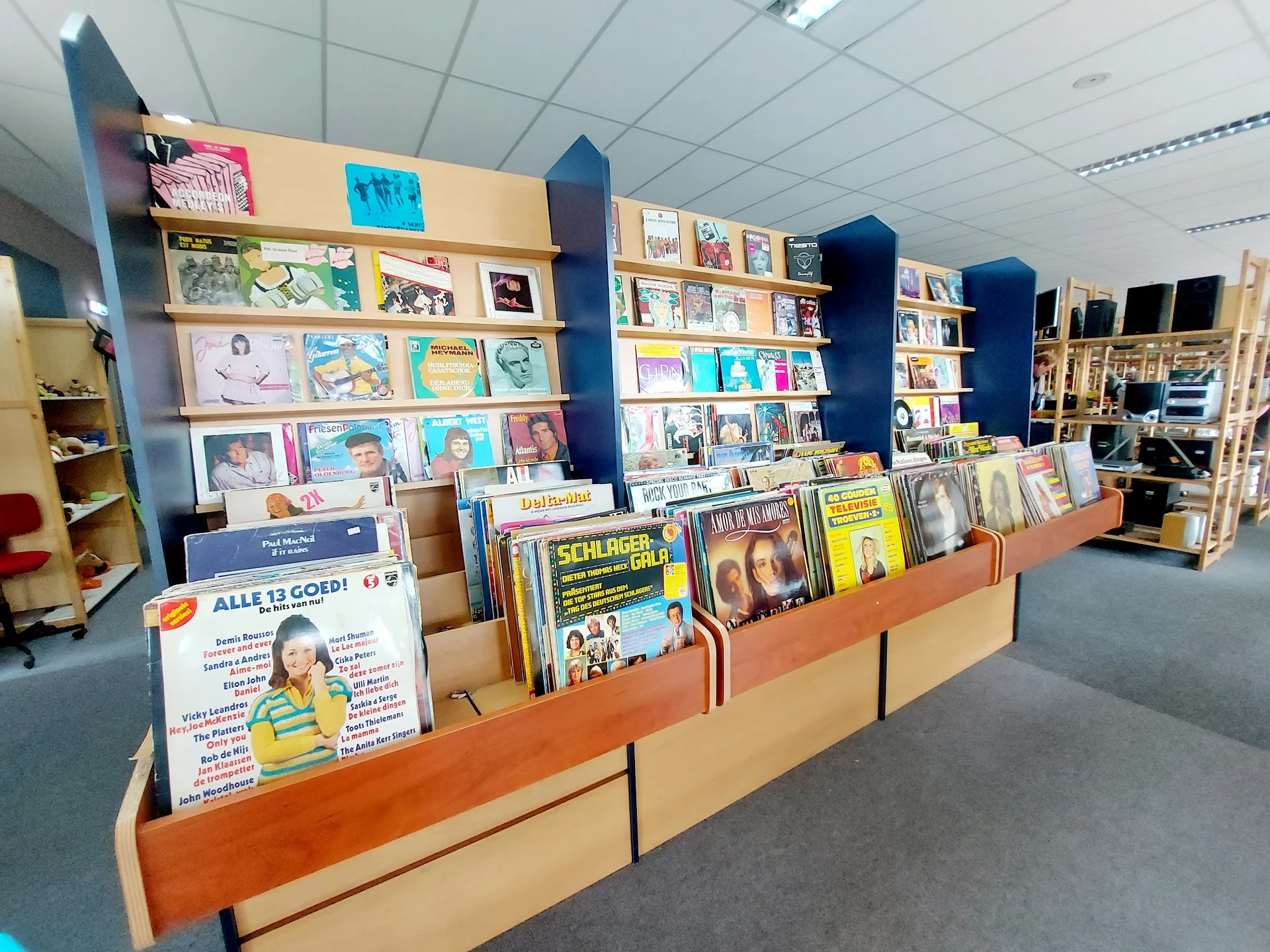 Winkelinterieur met houten display-kasten vol met boeken, dvd's en media tegen blauwe wandpanelen.