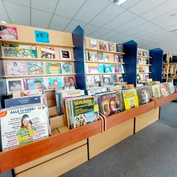 Winkelinterieur met houten display-kasten vol met boeken, dvd's en media tegen blauwe wandpanelen.