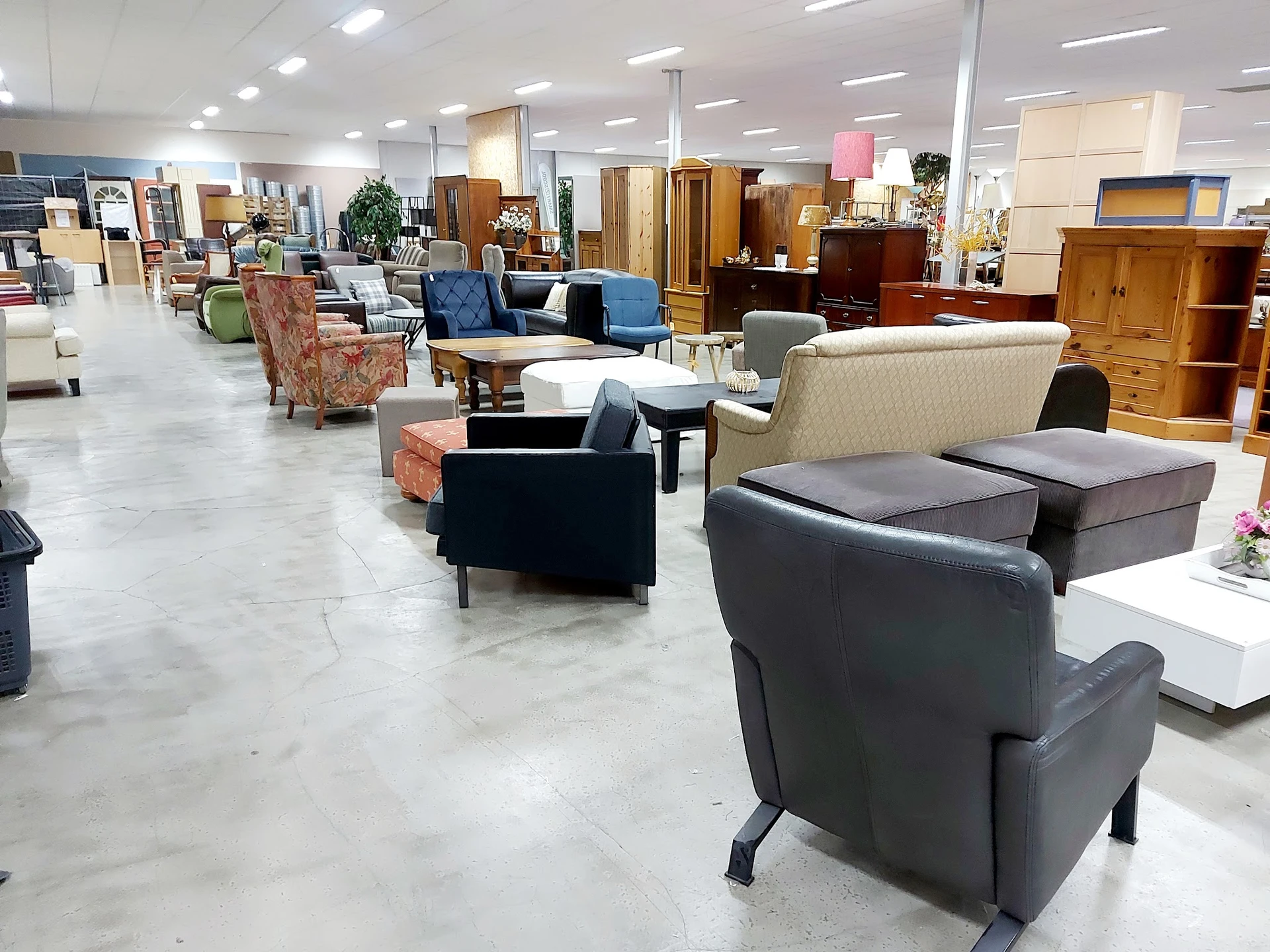 Ruime winkelvloer met diverse meubels uitgestald: fauteuils, banken, tafels en houten kasten.