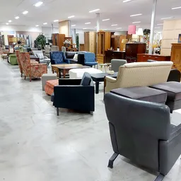 Ruime winkelvloer met diverse meubels uitgestald: fauteuils, banken, tafels en houten kasten.