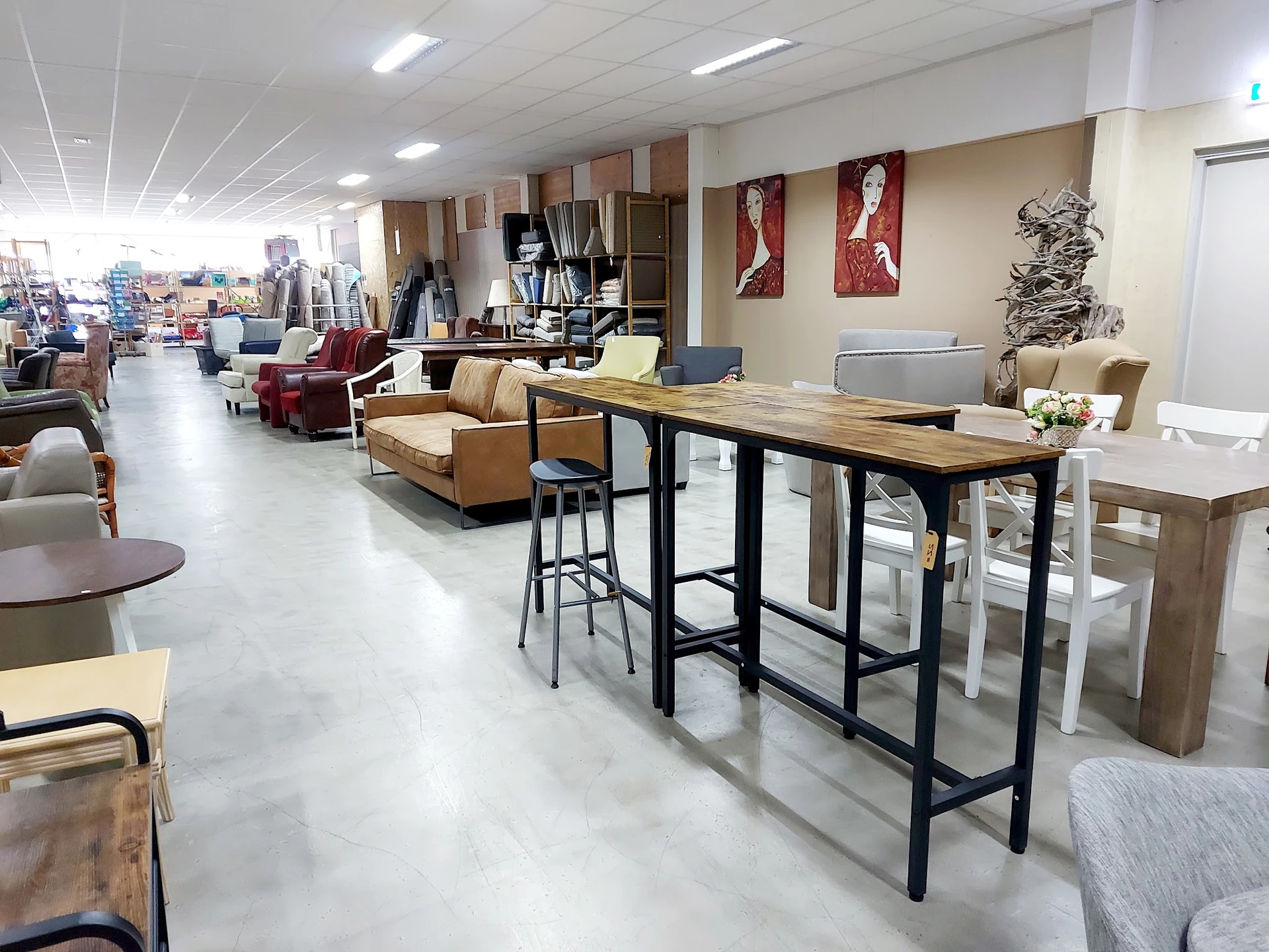 Winkelvloer met diverse meubels: barkruk bij houten bartafel, bruine fauteuils, decoratieve objecten en kasten op stellingen