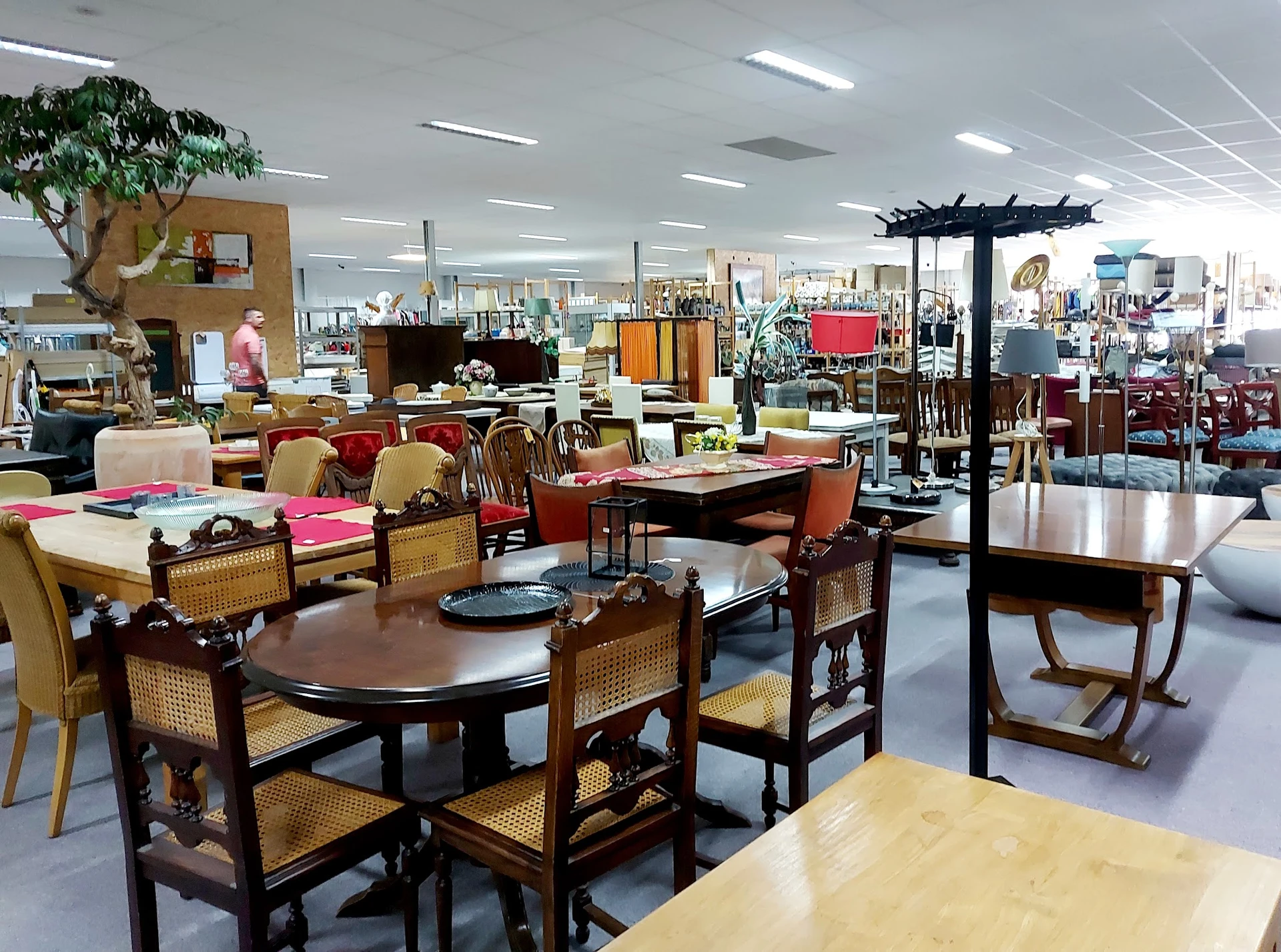 Overzicht van de winkelvloer met houten eettafels, stoelen en diverse meubels in een kringloopwinkel