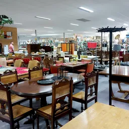 Overzicht van de winkelvloer met houten eettafels, stoelen en diverse meubels in een kringloopwinkel