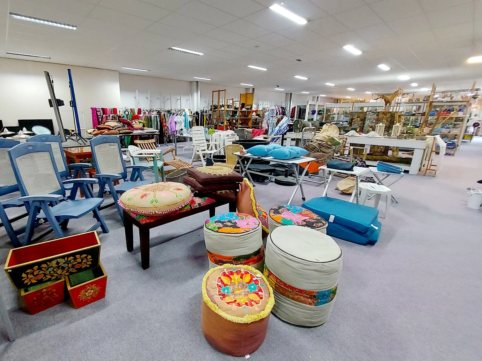 Ruim interieur van kringloopwinkel met diverse meubels, stoelen, trommels en huishoudelijke artikelen