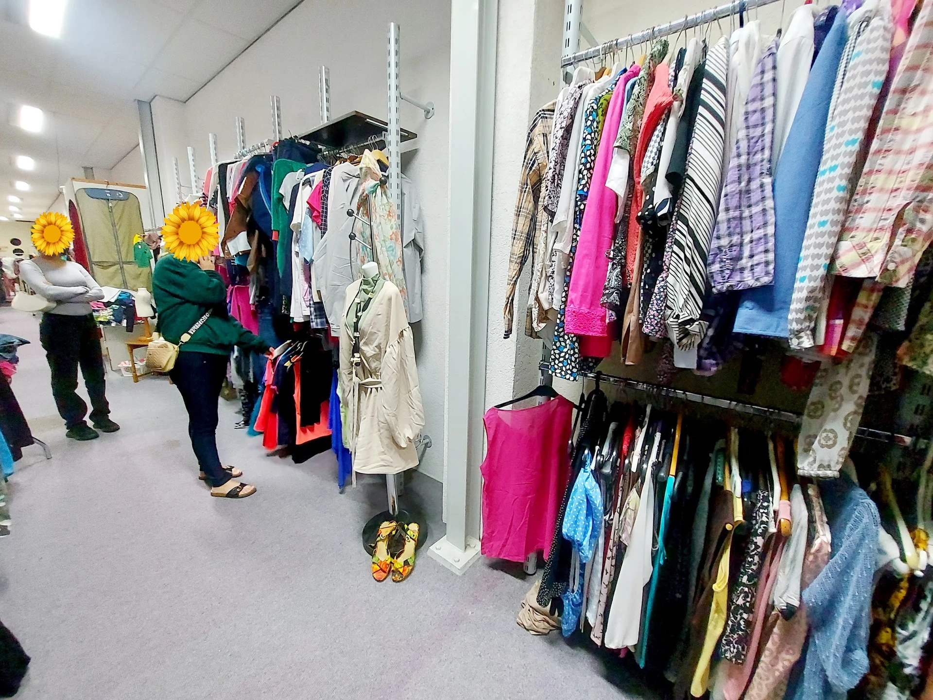 Winkelinterieur met rekken vol tweedehands kleding aan hangers, klanten aan het winkelen