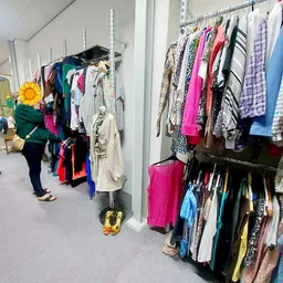 Winkelinterieur met rekken vol tweedehands kleding aan hangers, klanten aan het winkelen