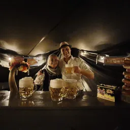 Twee mannen in Tiroler kledij achter een toog met biertappen en gevulde bierglazen