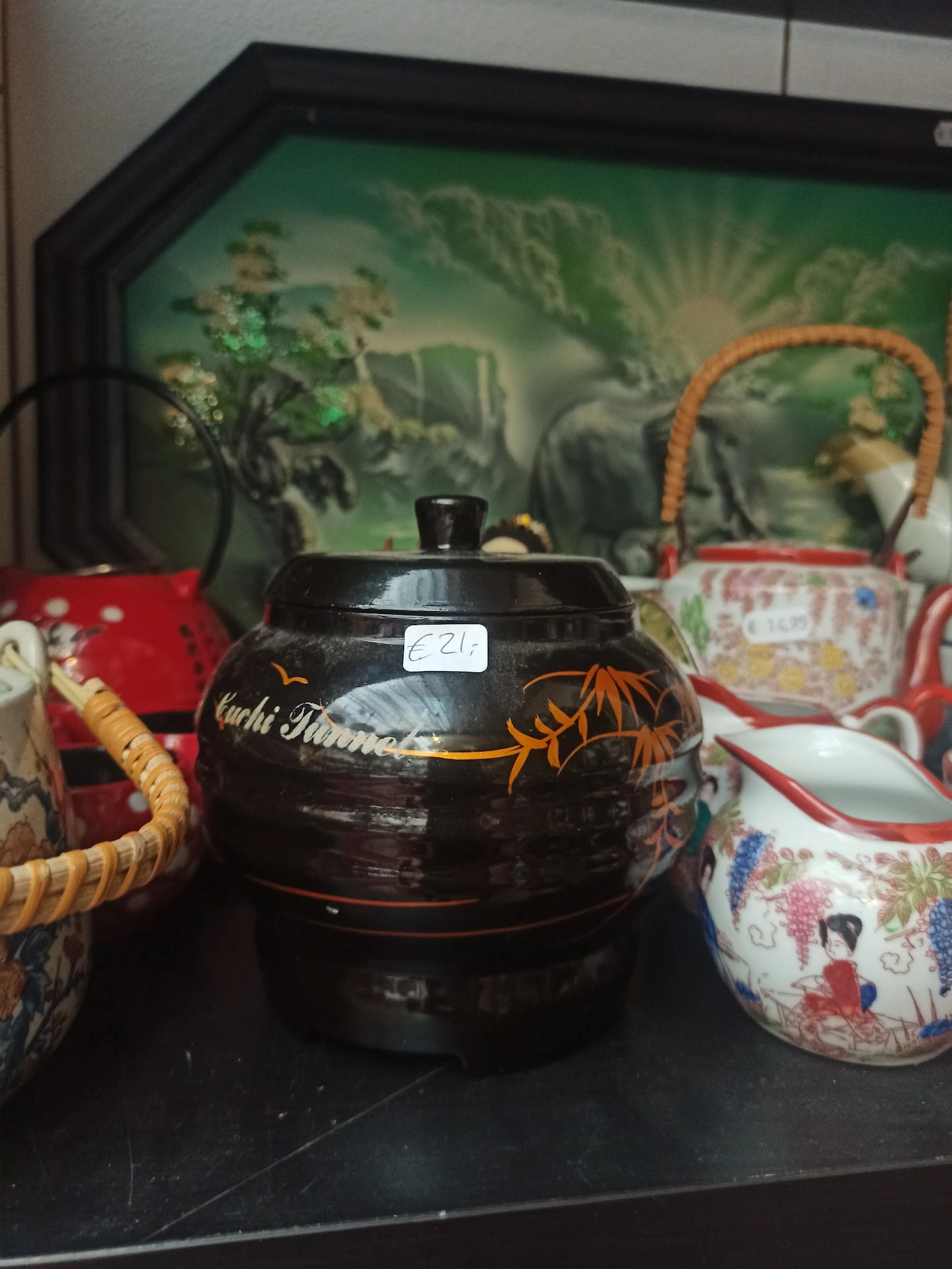 Zwarte theepot met gouden decoratie en houten handvat op tafel met decoratieve tassen op achtergrond