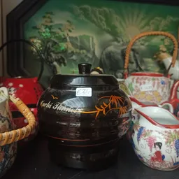 Zwarte theepot met gouden decoratie en houten handvat op tafel met decoratieve tassen op achtergrond