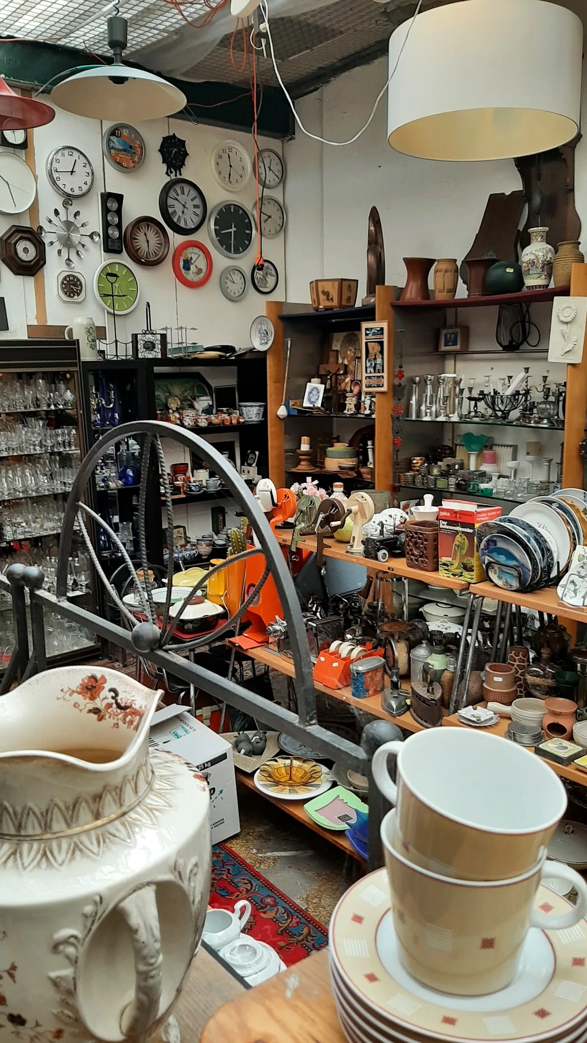 Volle werkplaats met stellingen, gereedschap, fietswiel en diverse voorwerpen op tafel en planken