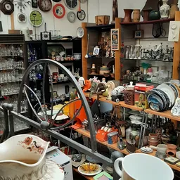 Volle werkplaats met stellingen, gereedschap, fietswiel en diverse voorwerpen op tafel en planken