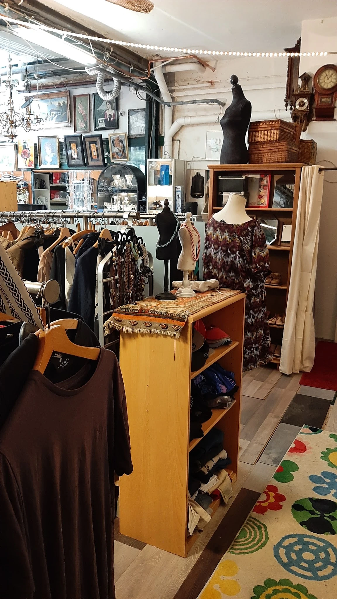Interieur van kringloopwinkel met kledingrekken, etalagepop met bruine jurk en houten displaytafel met sjaals