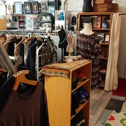 Interieur van kringloopwinkel met kledingrekken, etalagepop met bruine jurk en houten displaytafel met sjaals