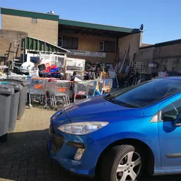 Buitenopstelling met diverse gebruikte artikelen, winkelkarrussen, elektronics en huishoudelijke spullen