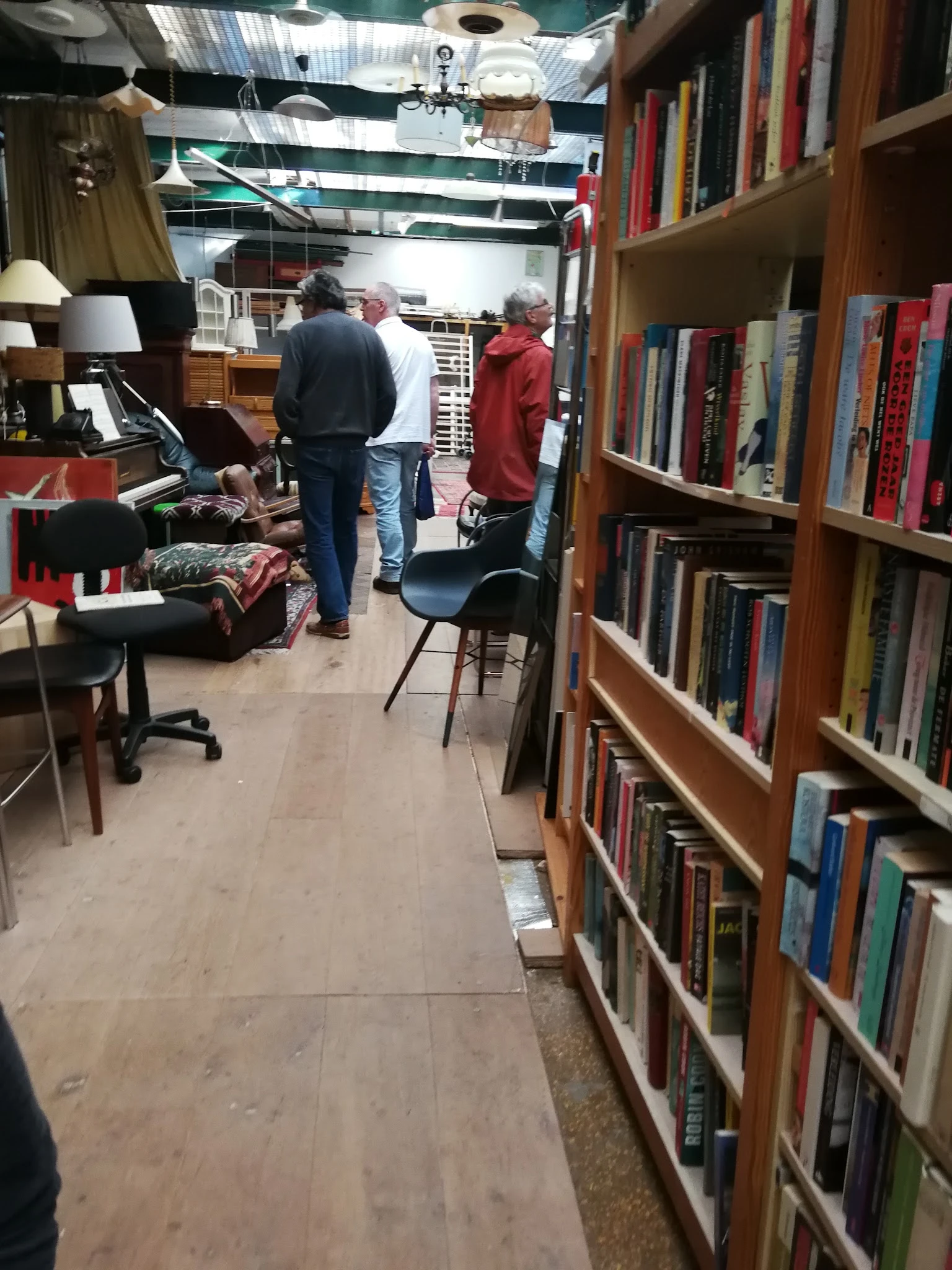 Binnenzicht van kringloopwinkel met boekenrekken, bezoekers en diverse spullen