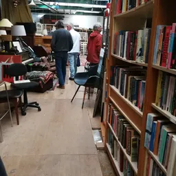 Binnenzicht van kringloopwinkel met boekenrekken, bezoekers en diverse spullen
