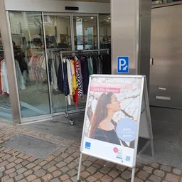Winkelpui met glazen deuren en tweedehands kleding aan rekken, parkeerplaatsbord en promotiebord op straat
