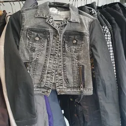 Tweedehands jassen en jasjes op hangers, waaronder een grijze spijkerjasje in het centrum