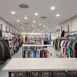Overzicht van de winkelvloer met rekken vol tweedehands kleding voor mannen, vrouwen en kinderen, verlicht plafond met LED-sp