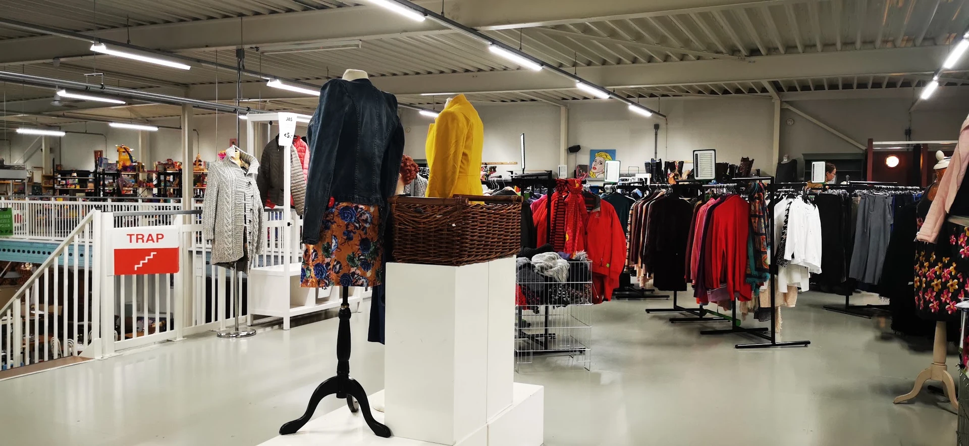 Rekken met tweedehands kleding in verschillende kleuren, waaronder rode jassen en zwarte kledingstukken op standaards en kaps