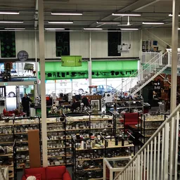 Overzicht van kringloopwinkel met meerdere verdiepingen, stellingen vol spullen, trappen en reling zichtbaar