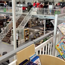 Overzicht van meerdere verdiepingen in een kringloopwinkel met trappen, stellingen met spullen en diverse huisraad